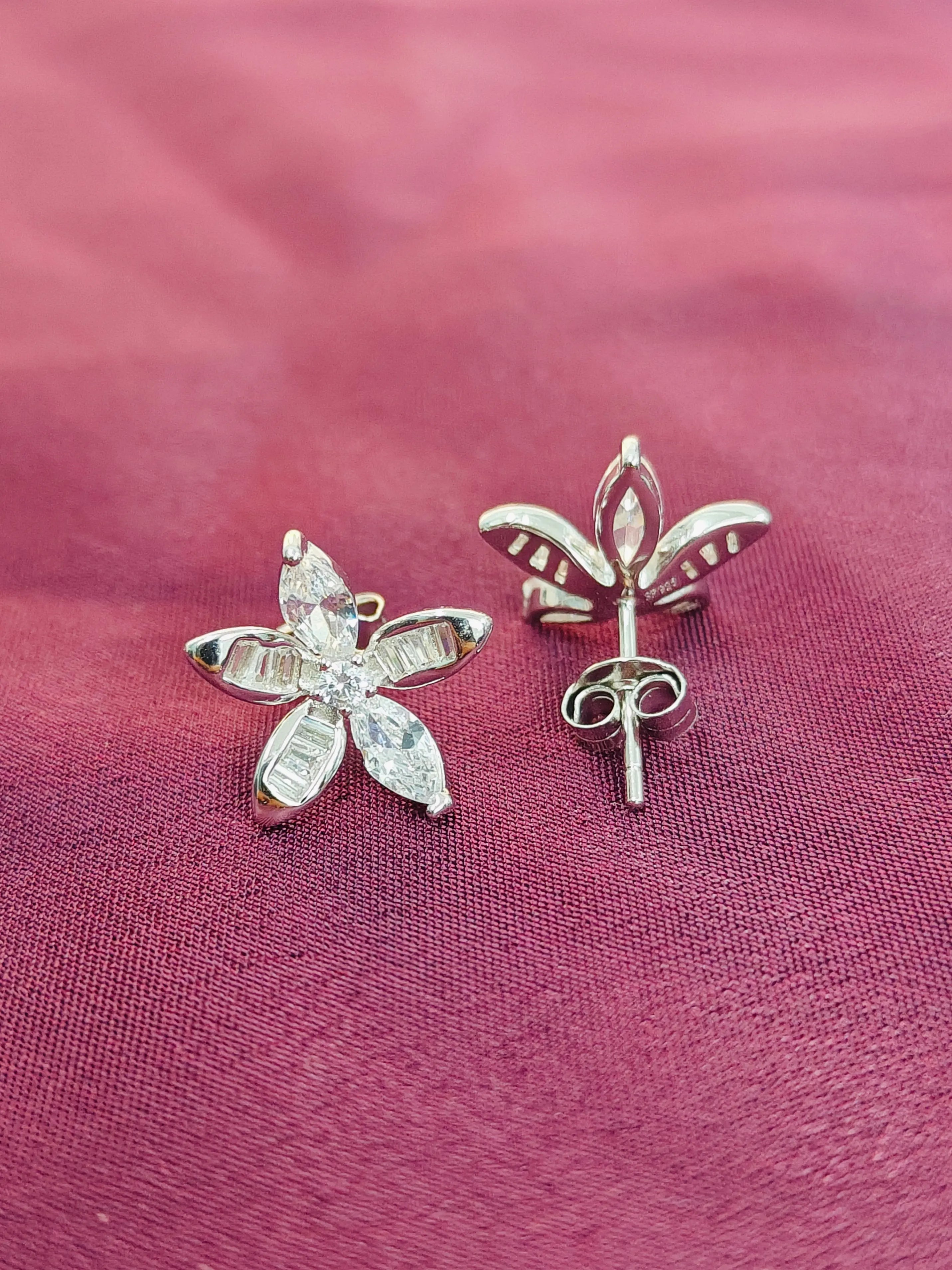 Silver flower-shaped earrings on a pink fabric background